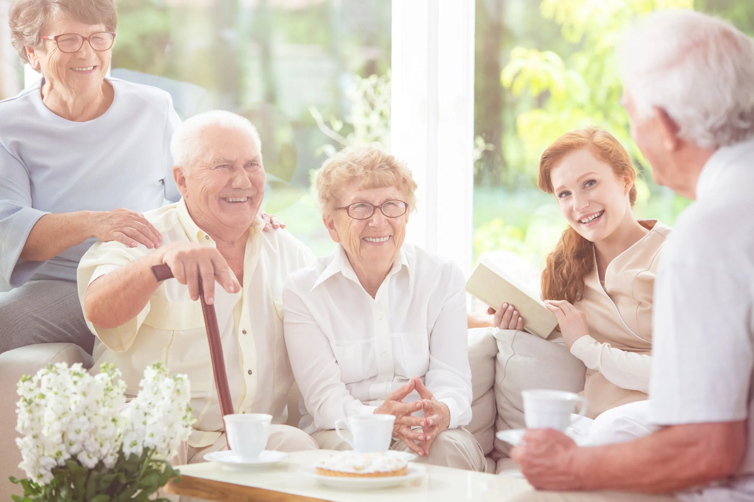 Smiling senior people and happy caregiver drinking tea in the nursing house
