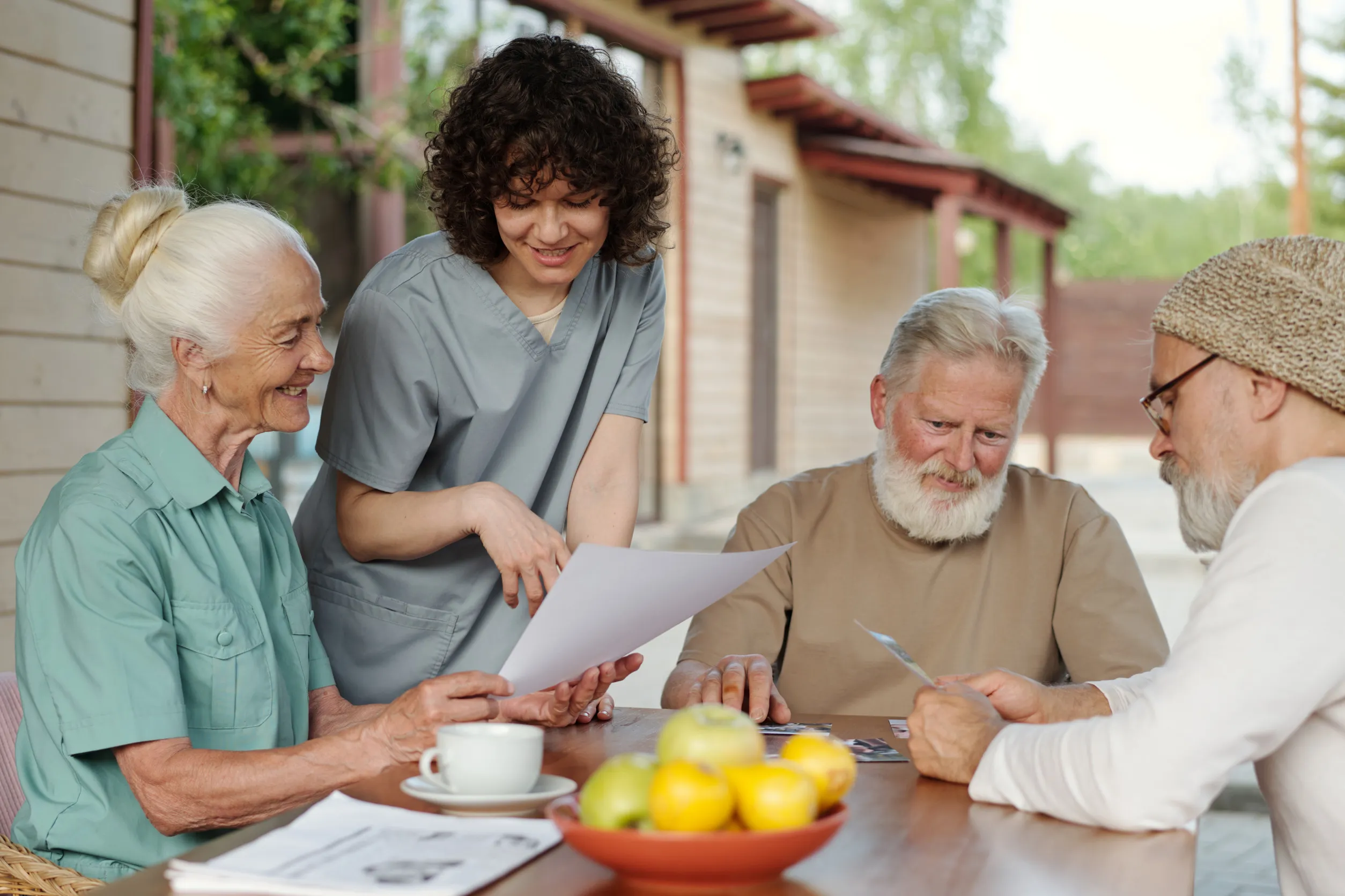 Young female caregiver explaining data in document to senior female patient of retirement home while bending over her during conversation